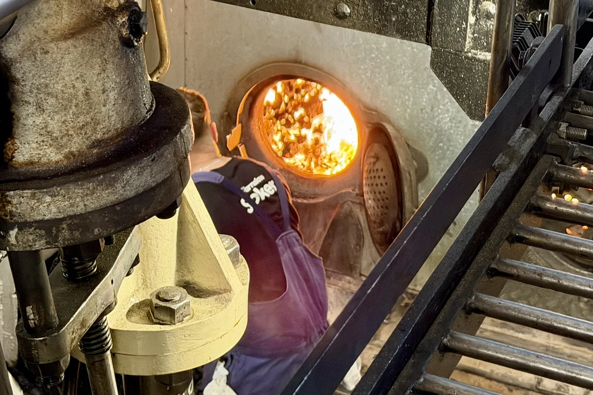 A stoker feeding coal into the open firebox of a coal-fired steamship's boiler