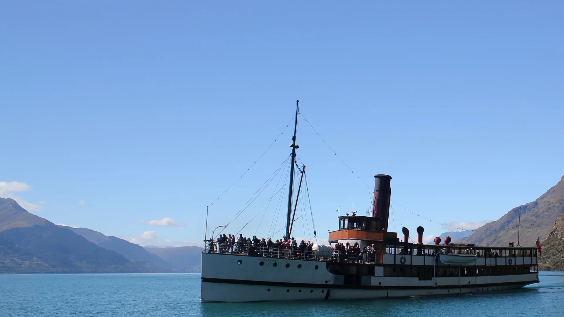 The TSS Earnslaw steamship, its funnel and rigging whole and clear, crossing Lake Wakatipu toward Walter Peak with the Remarkables behind
